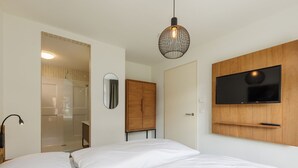 A modern bedroom with a bed, a TV mounted on the wall, and a shower area visible through a glass door. - Holiday Home in Bad Bentheim Near Dutch Border (Bad Bentheim)