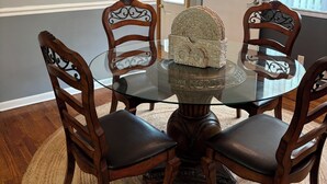 A dining area with a round glass table surrounded by wooden chairs, a woven rug, and decorative wall art. - Charming 3-Bedroom Yellow Ranch Retreat near Lake Michigan (Benton Harbor)