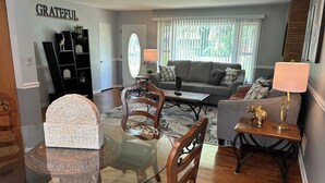 A living room with a glass dining table, a sofa, a coffee table, and a bookshelf. - Charming 3-Bedroom Yellow Ranch Retreat near Lake Michigan (Benton Harbor)