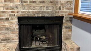 A brick fireplace with a wooden mantel and a window above it. - Charming 3-Bedroom Yellow Ranch Retreat near Lake Michigan (Benton Harbor)