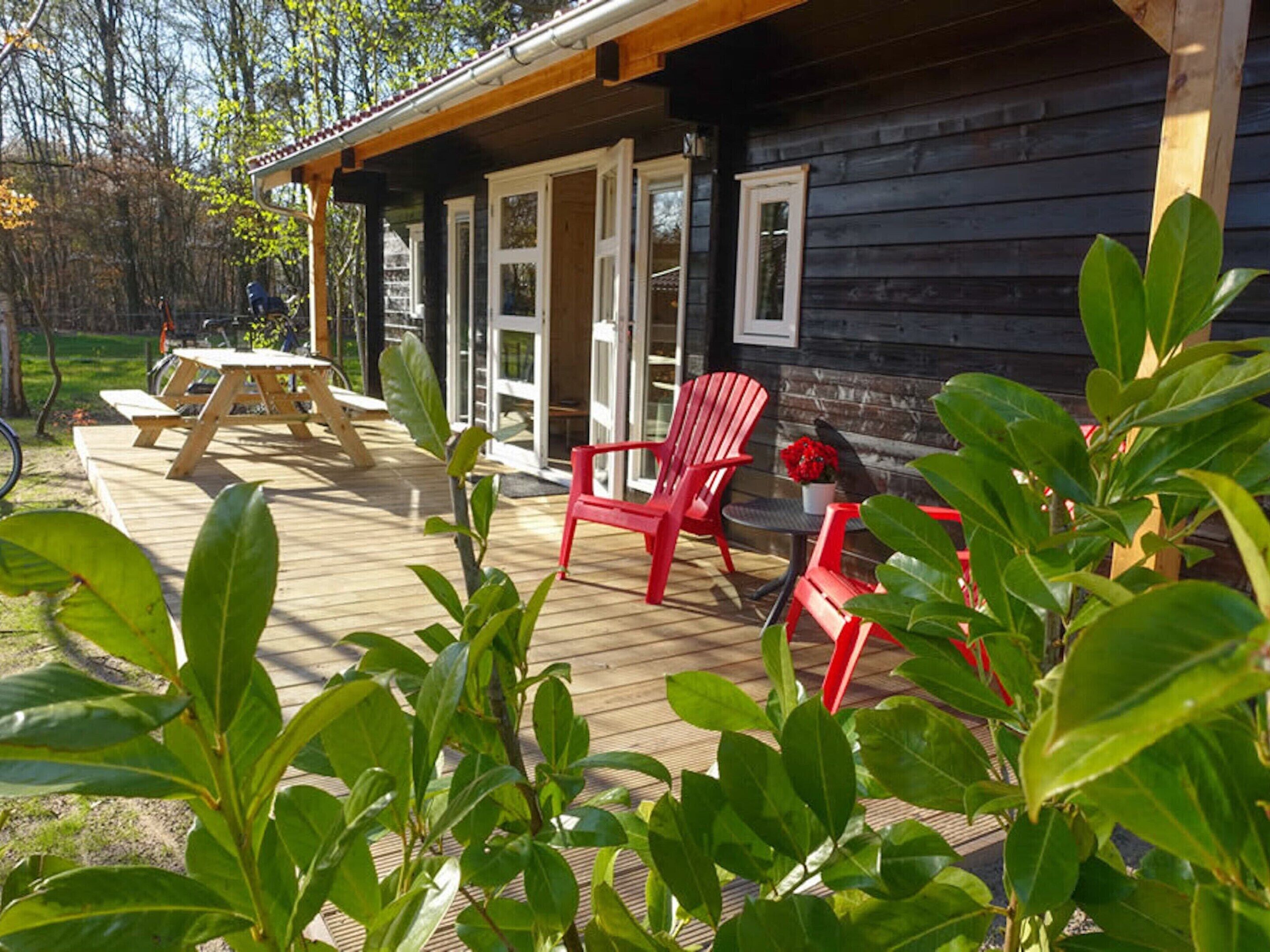 A wooden cabin with a deck, red chairs, and a picnic table.