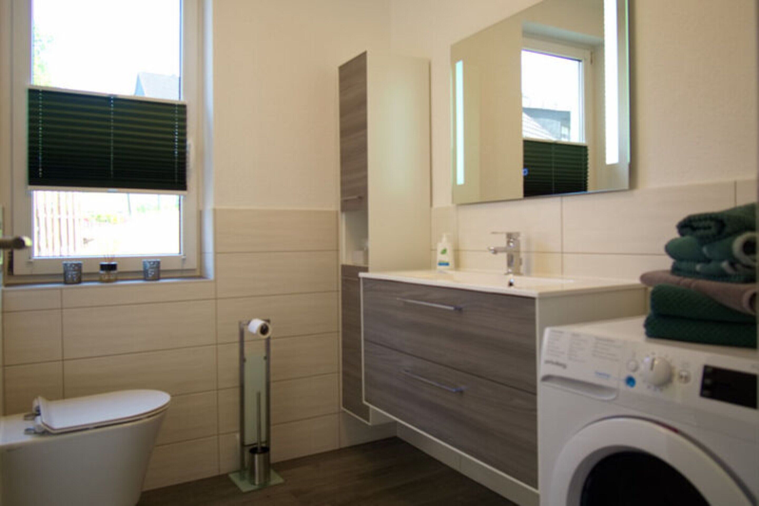 Een moderne badkamer met toilet, wastafel, spiegel en een wasmachine.