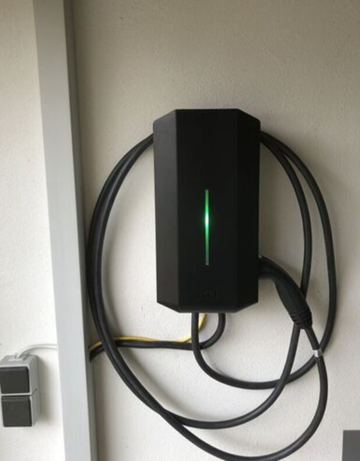 A black electrical outlet with a green light indicator, connected to multiple black cables.
