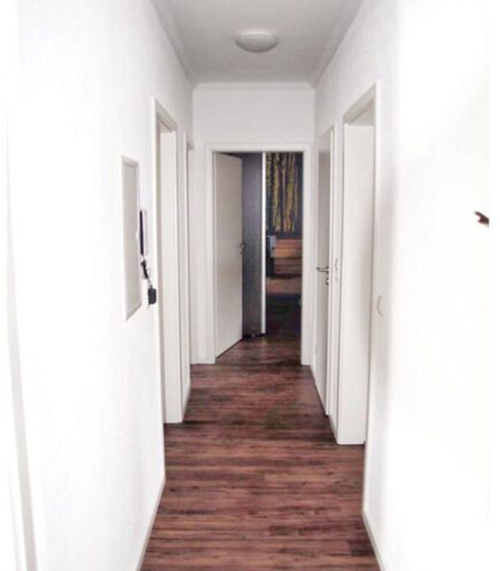A narrow hallway with wooden flooring and white walls.