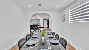 Un comedor con una mesa larga dispuesta para seis personas, rodeada de sillas, y una planta en maceta en el centro.