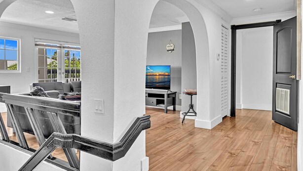 Una sala de estar moderna con un televisor grande, piso de madera y una escalera con barandilla negra.
