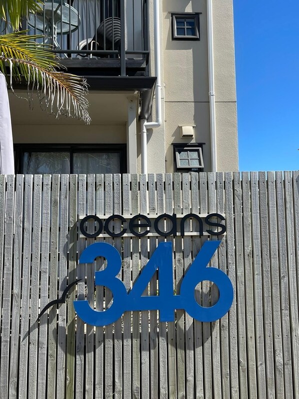 Une clôture en bois portant l’inscription « oceans 346 » et un balcon agrémenté d’un palmier.