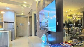 Uma sala de estar moderna com televisão de tela plana, sofá, mesa de centro com livros e área de jantar com cadeiras e lustre.