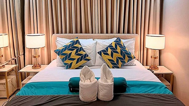 Quarto de hotel com cama, duas mesas de cabeceira, luminárias, cabeceira e cortinas.