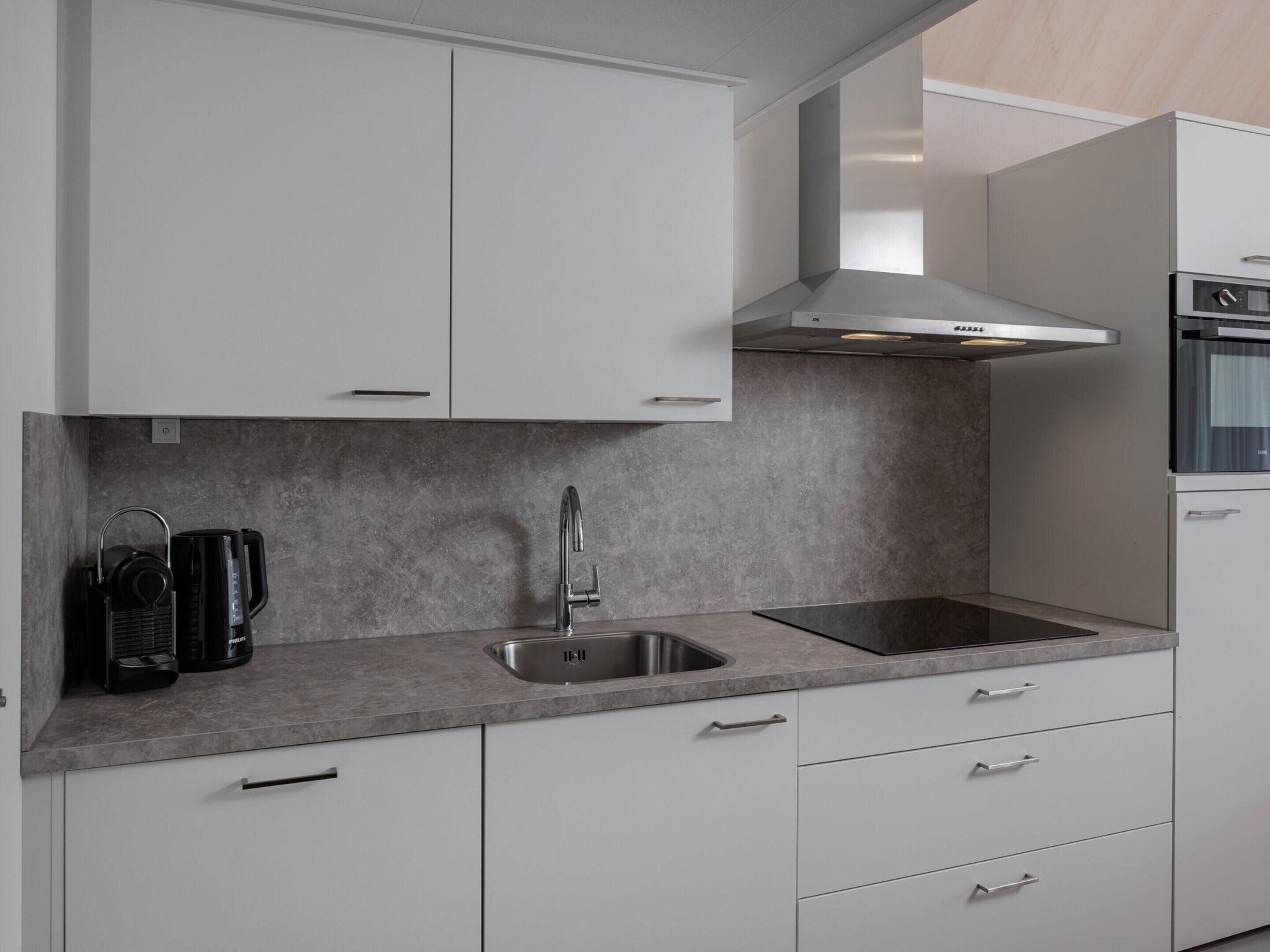 Eine moderne Küche mit weißen Schränken, einer Edelstahlspüle und einem eingebauten Backofen.