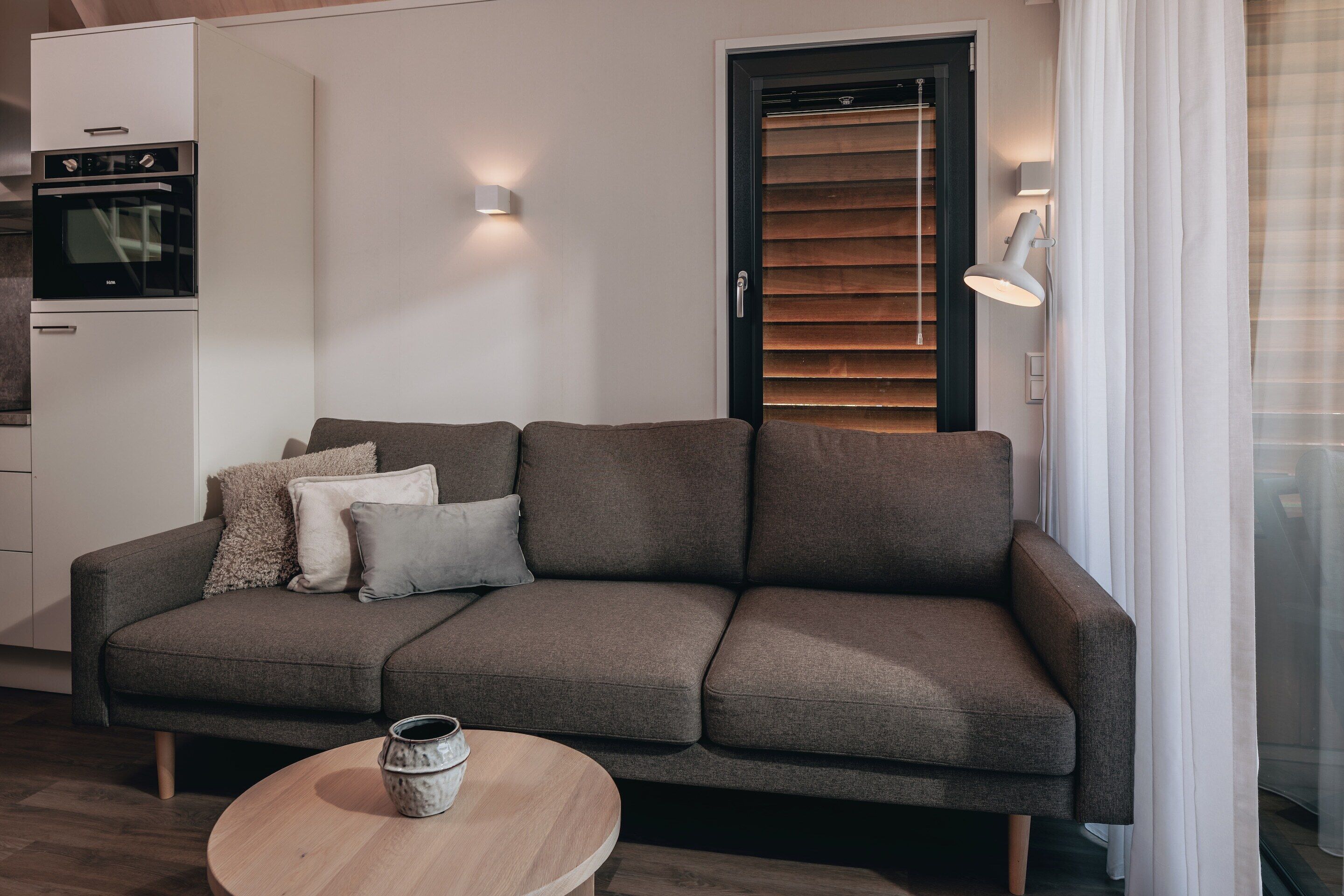 A modern living room with a sofa, a round wooden table, and a built-in oven.