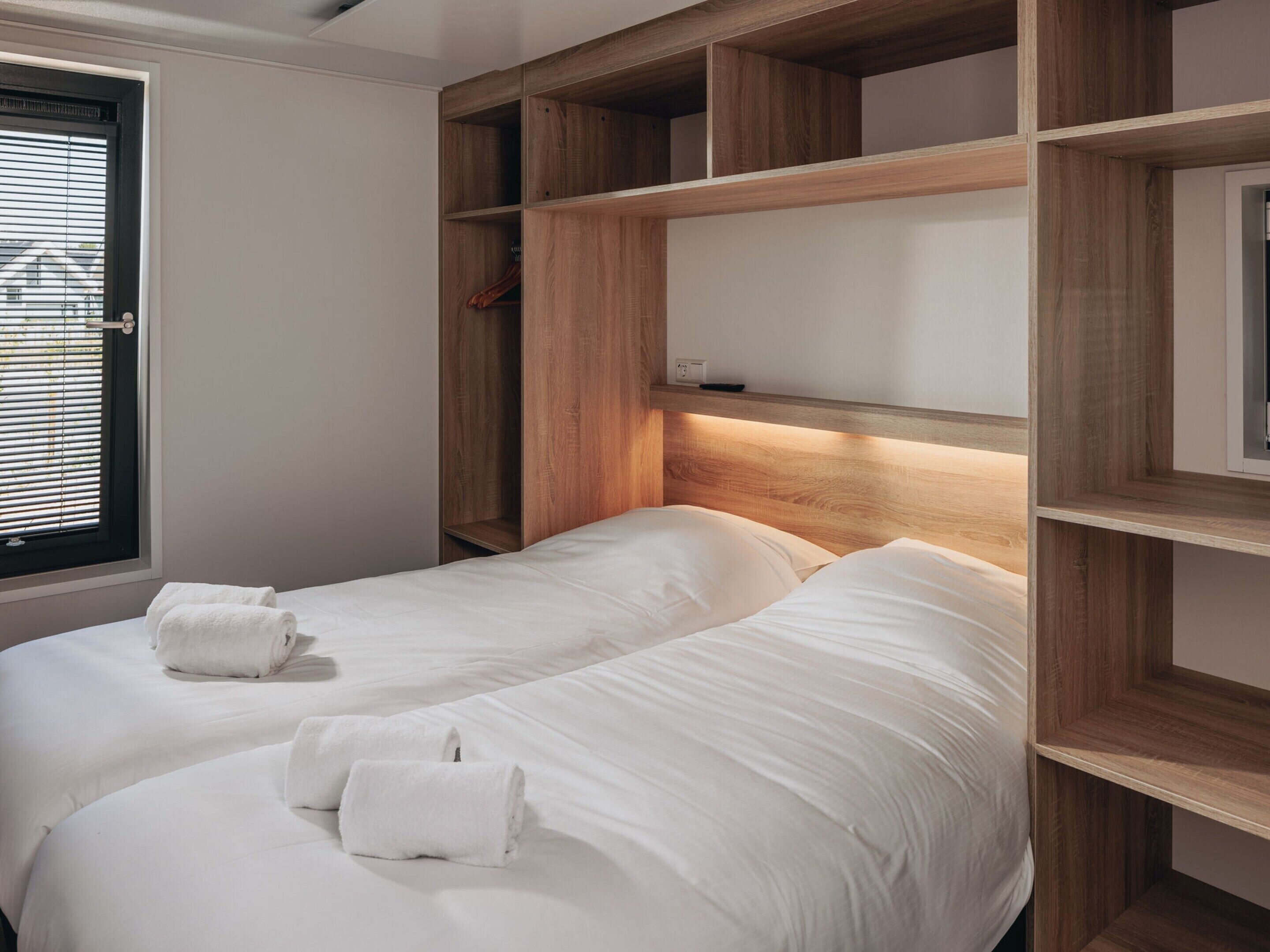 A bedroom with two beds, wooden headboards, and a window with blinds.