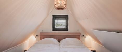 A bedroom with two beds, a wooden headboard, bedside lamps, a window with blinds, and a hanging light fixture.