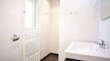 A modern bathroom with white tiles, a white radiator, a window, and a sink with a mirror.