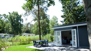 Ein kleines Haus mit Terrasse, umgeben von Rasen und Bäumen.