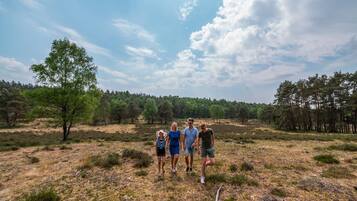 Een groep mensen staat in een natuurlandschap met bomen en open velden.
