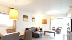 Ein modernes Wohnzimmer mit Essbereich, ausgestattet mit einer Couch, Sesseln, einem Couchtisch und Kunstwerken an den Wänden.