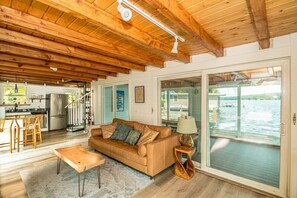 A spacious living room with a wooden ceiling, a sofa, a coffee table, and a view of a body of water through large sliding doors.