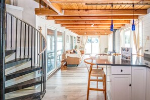 Un intérieur spacieux avec un escalier en bois, un coin cuisine et un espace de vie comprenant un canapé et une table à manger.
