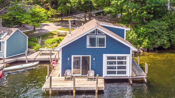 A houseboat with a dock, a covered deck, and a small porch with chairs. - Overwater Bliss | Private Dock + 4 Min to Sunapee (Newbury)