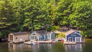 A waterfront property with docked boats, a small house, and a larger blue building. - Overwater Bliss | Private Dock + 4 Min to Sunapee (Newbury)
