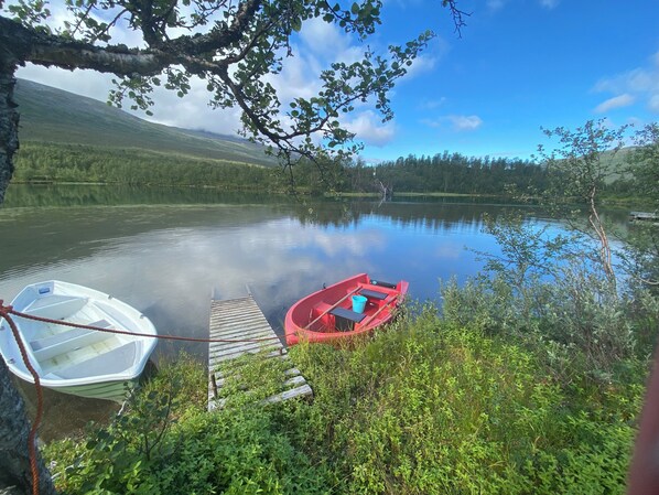 A tranquil lake with a wooden dock, a red boat, and a white boat. - Aurora Paradise house with PS5, WiFi, AC, 98 inch TV and private playground! (Nordland)