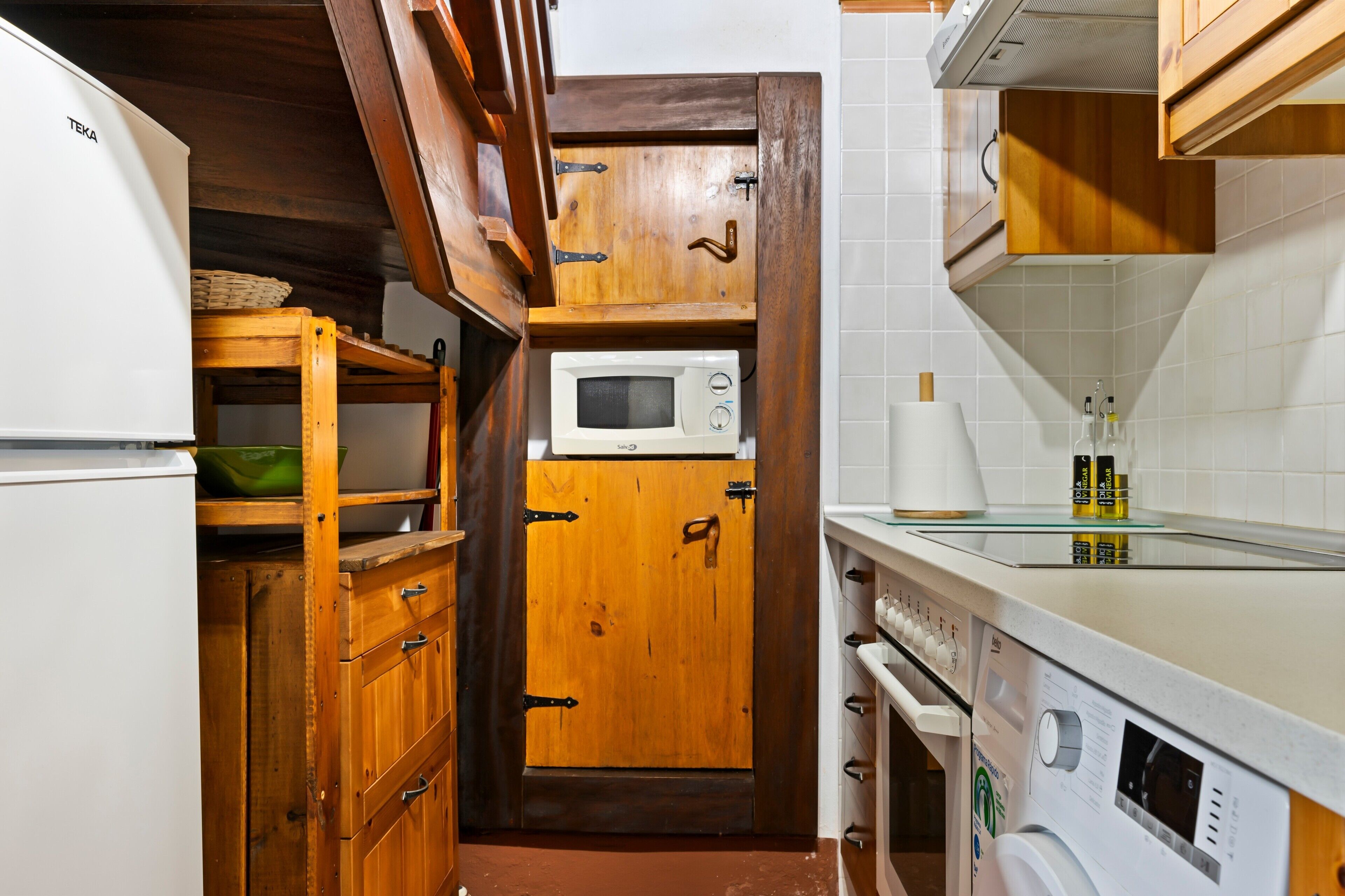Cocina compacta con microondas, armarios de madera y lavadora.