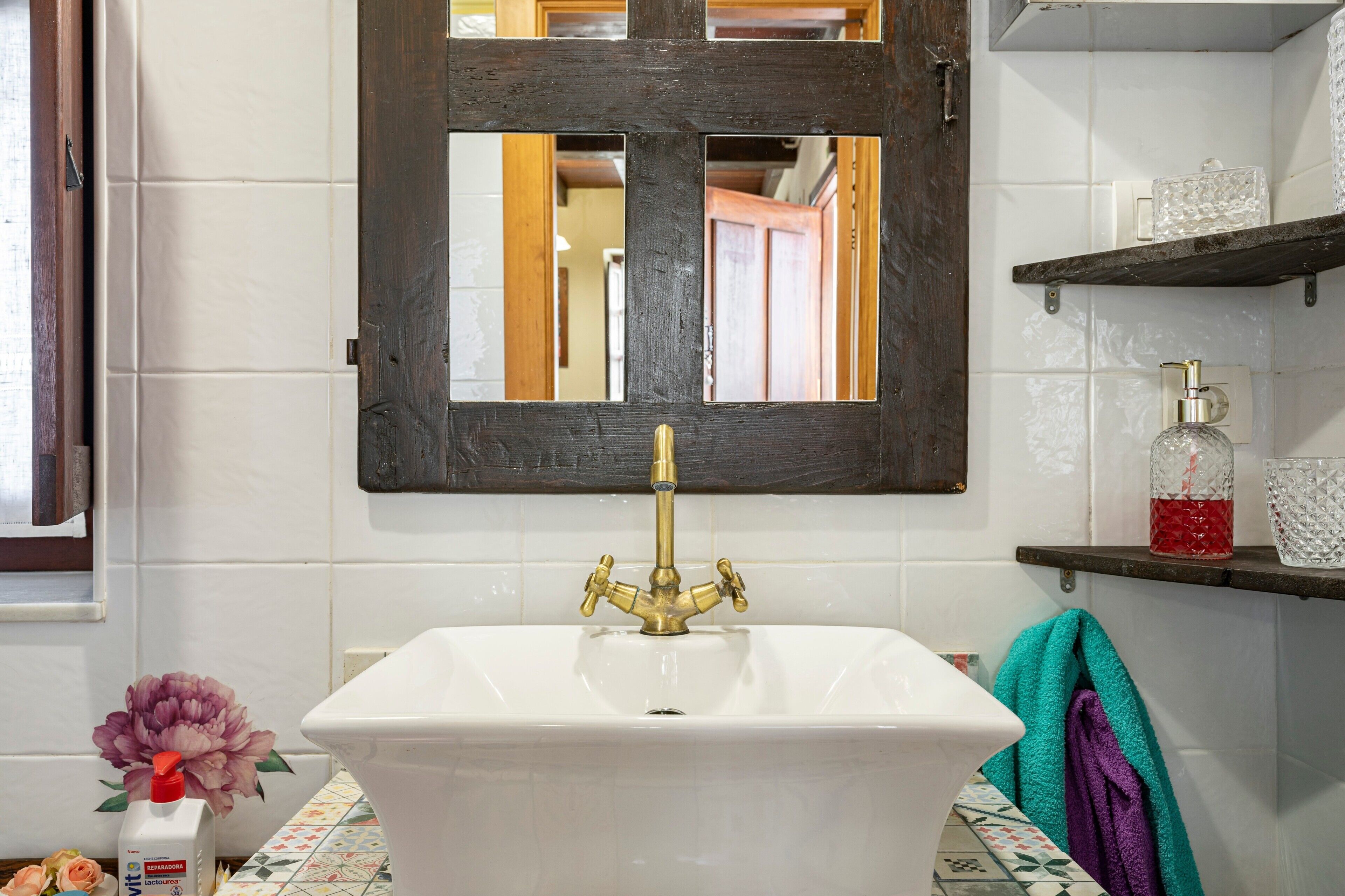 A bathroom with a white sink, a mirror, and a shelf with toiletries.