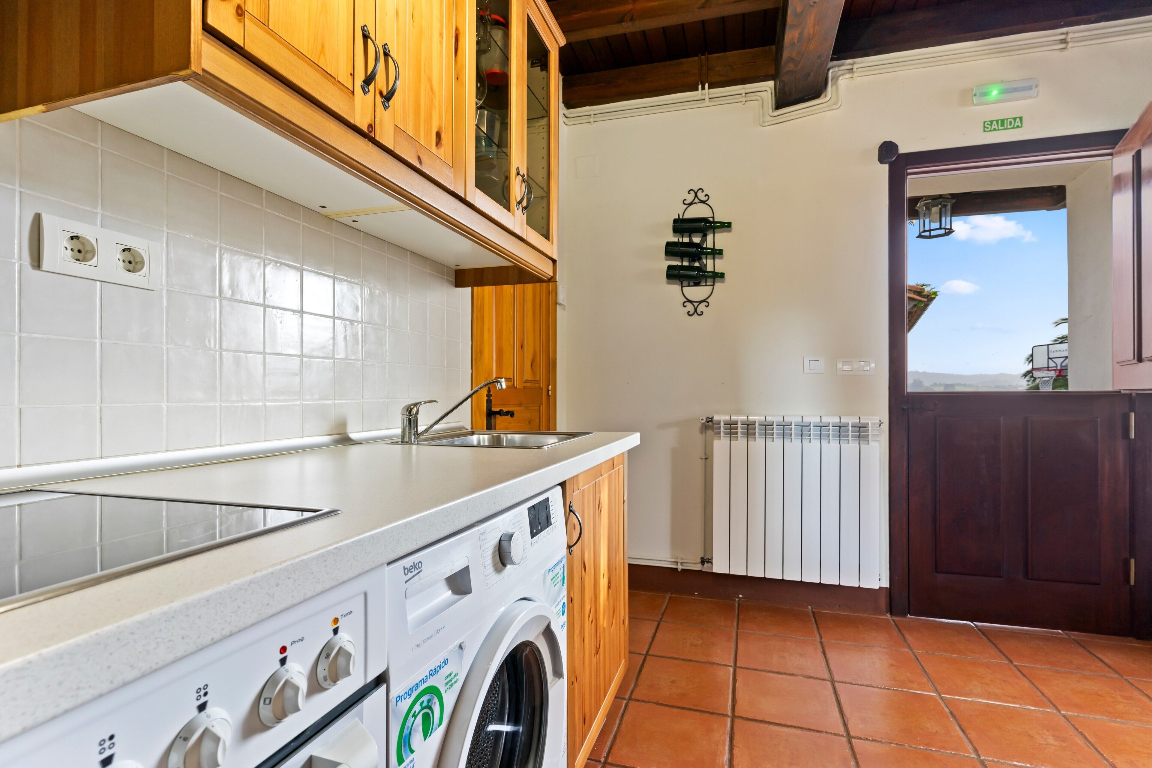 Een keuken met een wasmachine, houten kastjes, een spoelbak en een radiator.