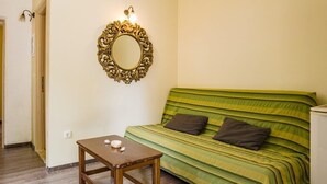 A room with a bed, a small table, a wall-mounted mirror, and a light fixture.