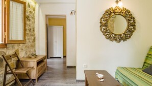 A room with a wooden desk, a chair, a bed with a green striped blanket, a mirror with an ornate frame, and a door leading to another room.