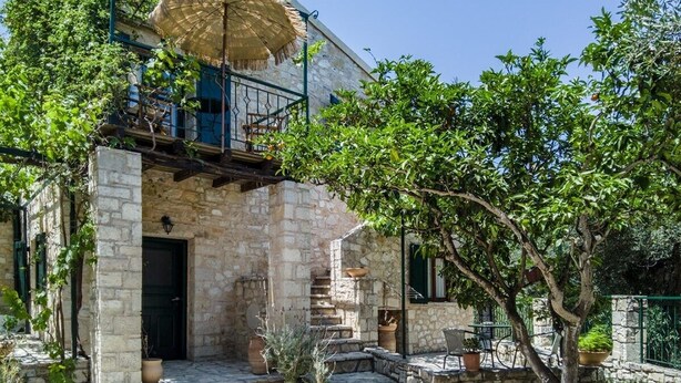 A stone building with a balcony, outdoor seating, and a thatched umbrella.