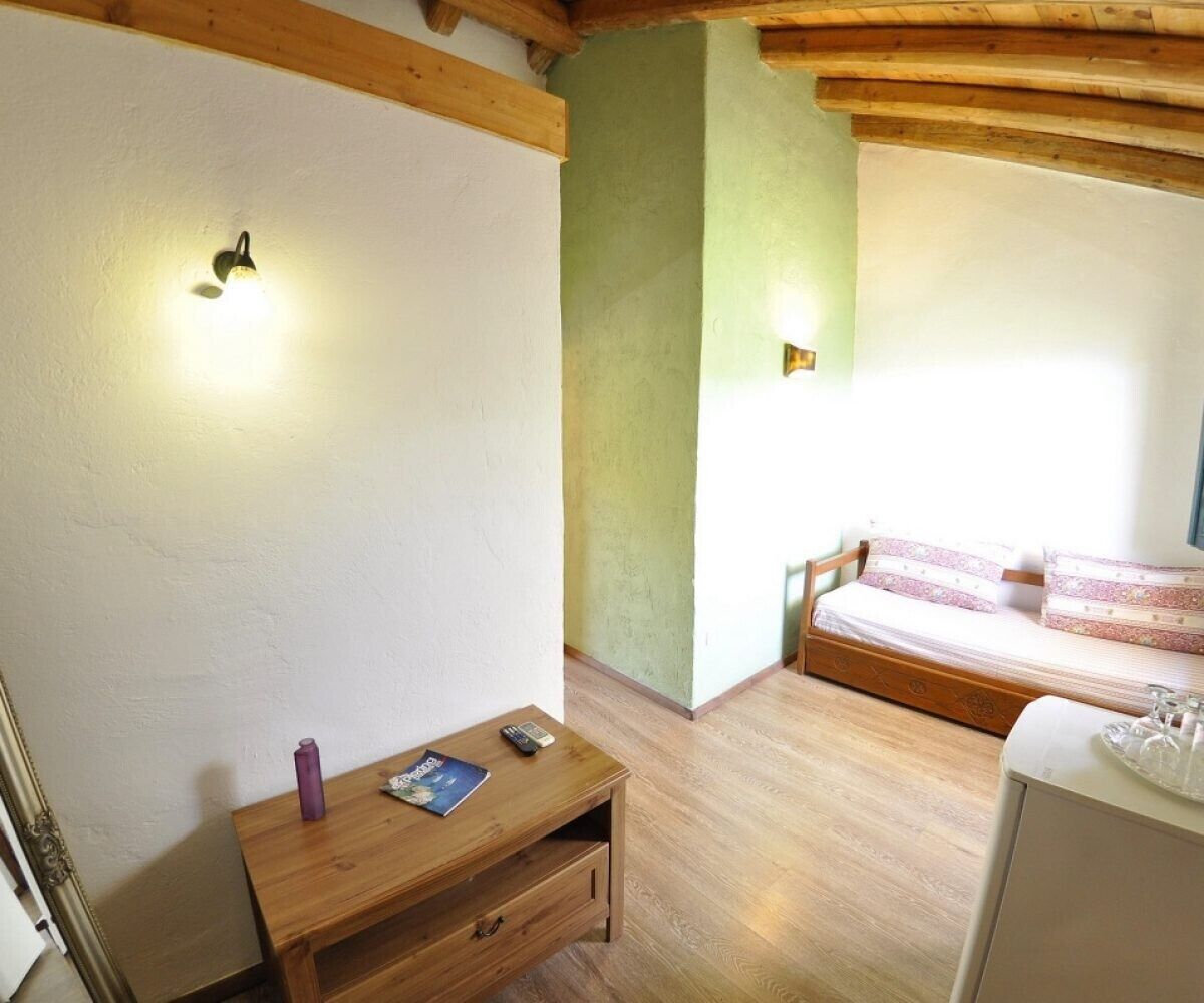 Une pièce comprenant un lit, une petite table en bois avec une télécommande et un magazine, ainsi qu’une armoire blanche.