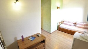Une pièce comprenant un lit, une petite table en bois avec une télécommande et un magazine, ainsi qu’une armoire blanche.