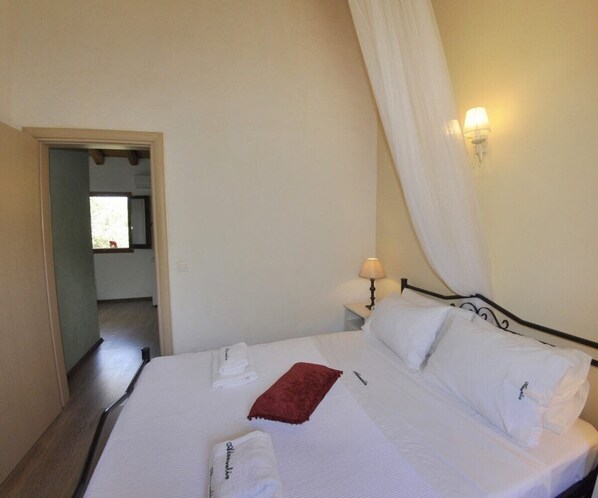Une chambre d’hôtel avec un lit, du linge de lit blanc, un plaid rouge, deux lampes de chevet et une fenêtre avec des rideaux.