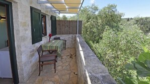 Un balcon dallé de pierre, avec une table et des chaises, une clôture en bois et une vue sur la verdure.