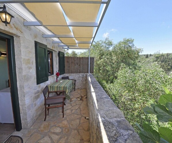 Un balcón con piso de piedra, una mesa y sillas, una valla de madera y vistas a zonas verdes.