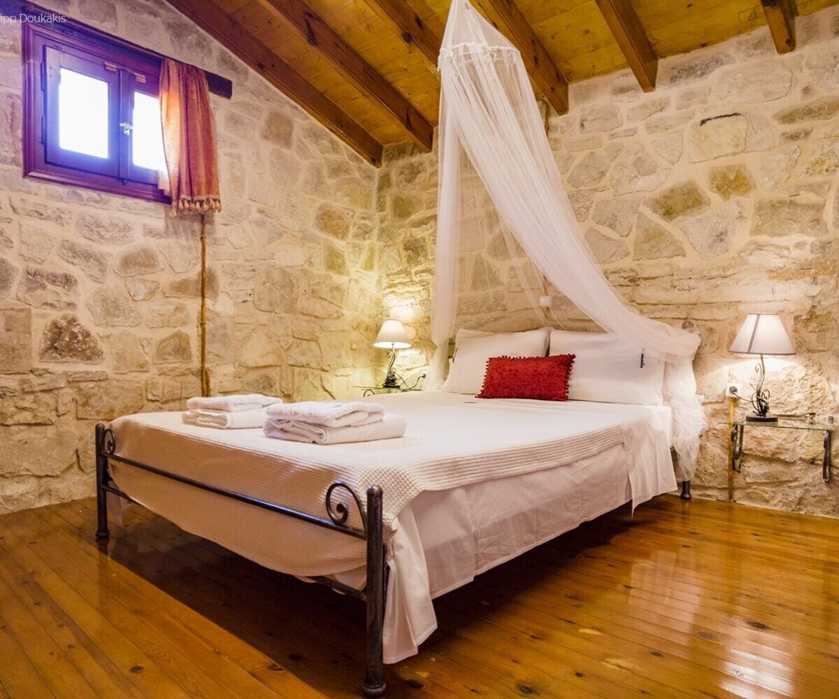 Une chambre aux murs de pierre, avec un lit, du linge de lit blanc, un baldaquin et deux lampes de chevet.