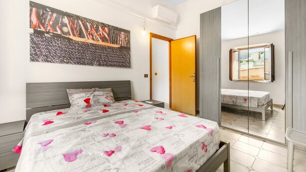 A bedroom with a large bed, a bedside table, a wardrobe, a mirror, and a painting on the wall. - Arbus Aventino Centrale Holiday Home with Private Terrace and Air Conditioning (Arbus)