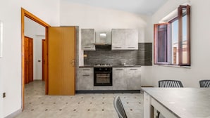 A modern kitchen with grey cabinets, a built-in oven, and a dining area with a table and chairs. - Arbus Aventino Centrale Holiday Home with Private Terrace and Air Conditioning (Arbus)
