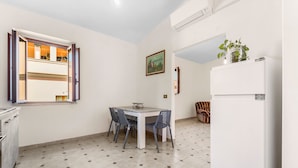 A kitchen with a dining table, chairs, a refrigerator, a window with open shutters, and a painting on the wall. - Arbus Aventino Centrale Holiday Home with Private Terrace and Air Conditioning (Arbus)