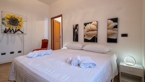 Ein ordentlich gemachtes Bett mit Handtüchern, ein Nachttisch mit Lampe und Wandbild.