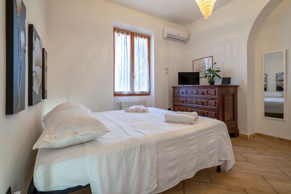Une chambre à coucher avec un lit, une commode, une télévision et une fenêtre avec des rideaux.