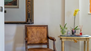 Ein Holzstuhl, ein kleiner Tisch mit einer Blumenvase und ein gerahmtes Bild an der Wand.