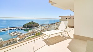 Un balcone con una sedia bianca, vista libera sul mare e un porto turistico con barche.