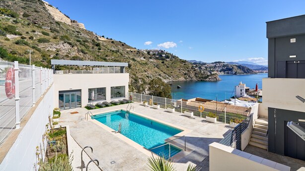 Un edificio moderno con piscina, vista sul mare e su una collina.
