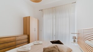 A bedroom with a bed, a wardrobe, a bedside table, and a window with curtains.