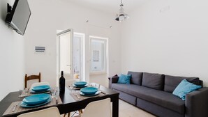 A dining area with a table set for two, a sofa, and a TV mounted on the wall.