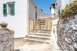 A narrow street with a stone wall and a white building with a wooden gate.