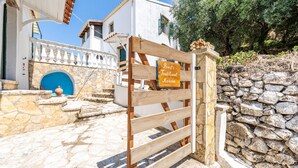 A stone pathway leading to a traditional wooden gate with a sign reading 'Priest's Traditional Mansion.' - Holiday Home 'Priest's Traditional Mansion' with Sea View, Shared Terrace and Wi-Fi (Corfu)